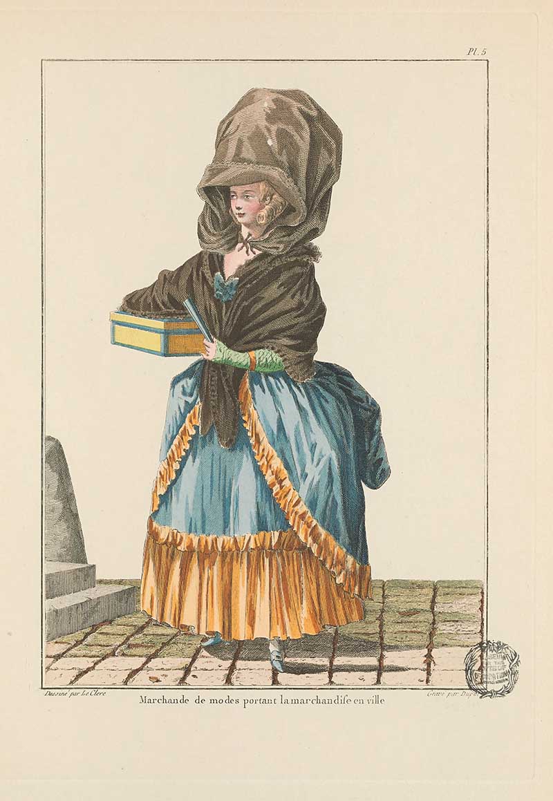 Fashion vendor in a blue and gold skirt with black shawl and oversized bonnet, carrying a small box on a cobbled street, French Galerie des Modes fashion print 18th century costume illustration