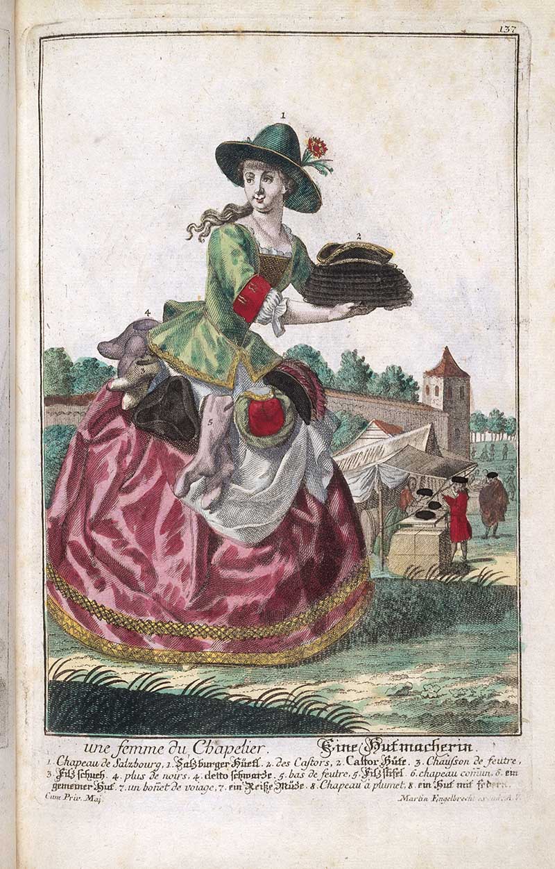 Antique costume print of a female hatter carrying stacked hats and hat forms, with a market stall and hat-making wares behind her.